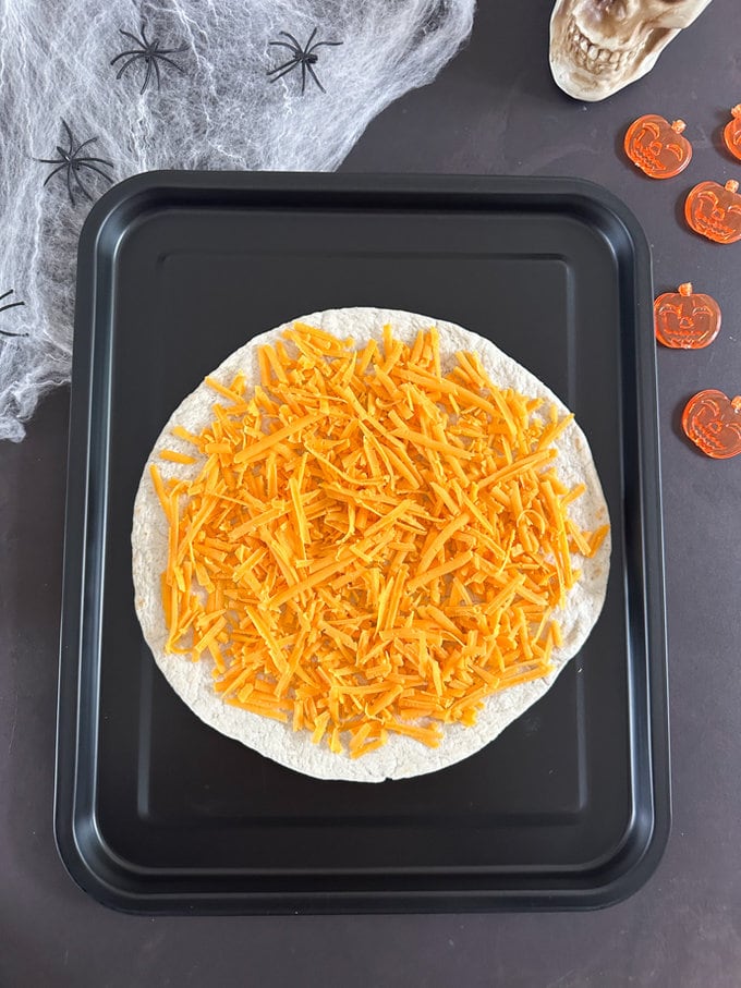 Tortilla being topped with lots of Delicious grated cheese. 