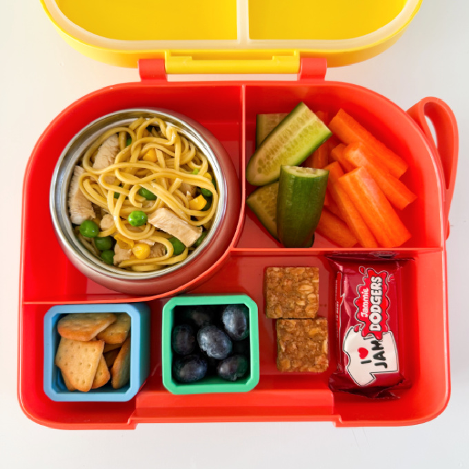 Chicken noodles served in a hot &  cold lunch box with sliced carrots and cucumber.